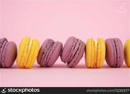 yellow, purple round baked macarons cakes on a pink background, dessert lies in a row, close up