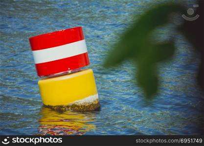Yellow red and white steel navigational floating buoy in the blue sea water.