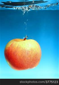 Yellow red apple in the water splash over blue background. Healthy food and active life. Square format