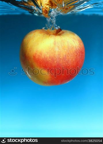 Yellow red apple in the water splash over blue background. Healthy food and active life. Square format.
