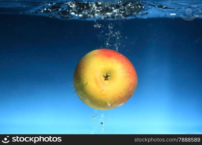 Yellow red apple in the water splash over blue background. Healthy food and active life.