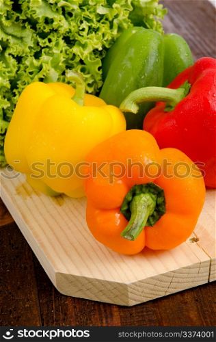 Yellow, red orange and green peppers, lettuce on wooden tray.