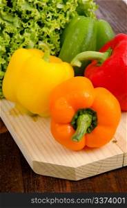 Yellow, red orange and green peppers, lettuce on wooden tray.