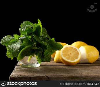 yellow ripe lemon and a bunch of fresh green mint on a wooden board, ingredients for lemonade, black background