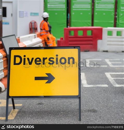 Yellow Road Sign with Arrow, Diversion: Barrier and Workers in background.. Yellow Road Sign with Arrow, Diversion: Barrier and Workers in background
