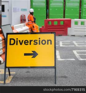 Yellow Road Sign with Arrow, Diversion: Barrier and Workers in background.. Yellow Road Sign with Arrow, Diversion: Barrier and Workers in background