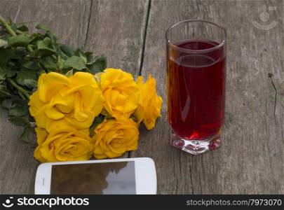 yellow roses, the mobile phone and glass of juice on a wooden table