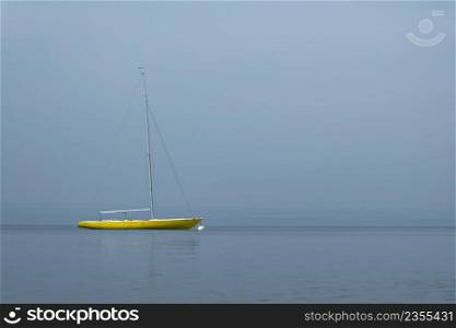 yellow sailboat lying at anchor in the fog