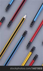Yellow sharp pencil tip in group of many pencil eraser heads on gray background in vertical frame for background design, concept of education, different ideas, conflict, originality with leadership