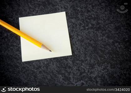 Yellow sticky note with a pencil against a dark marble background