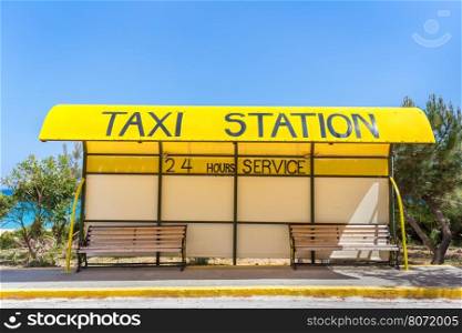 Yellow taxi station at coast in Greece with two benches
