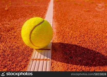 Yellow tennis ball touching the line on red clay court
