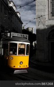 Yellow tram drives around bend through narrow street