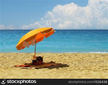Yellow umbrella on hot sandy beach by turquoise blue ocean. Beach gear
