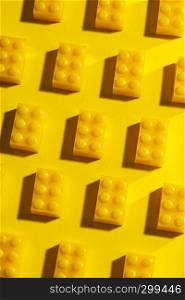 Yellow unicolour plastic geometric cubes. Construction toys on geometric shapes paper multi colored background. Arranged in rows. Children's toy. Circle geometric shapes on plastic bricks.