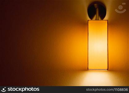 Yellow warm light from the wall lamp shining on aged cement wall in the dark room with copy space. Dark tone abstract wallpaper.