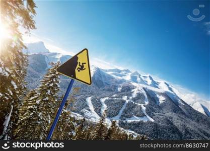 Yellow warning sign at a ski resort, ski slopes in the background