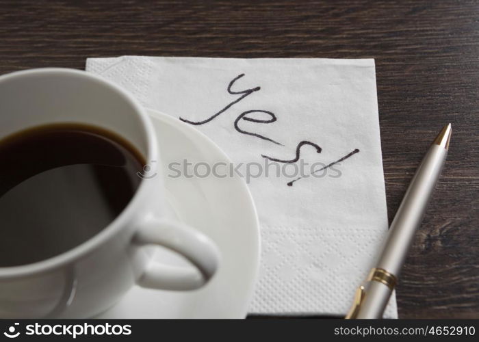 Yes answer on napkin. Yes message written on napkin and coffee cup on wooden table