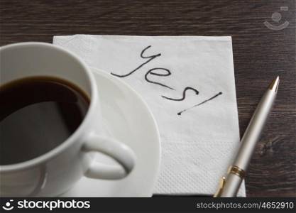 Yes answer on napkin. Yes message written on napkin and coffee cup on wooden table