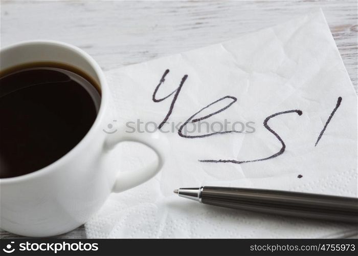 Yes answer on napkin. Yes message written on napkin and coffee cup on wooden table