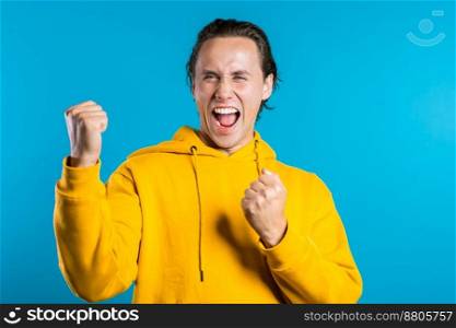 Yes winner gesture. Happy european man. Handsome guy with stylish hairdo surprised to camera over blue background. High quality photo. Yes winner gesture. Happy european man. Handsome guy with stylish hairdo surprised to camera over blue background