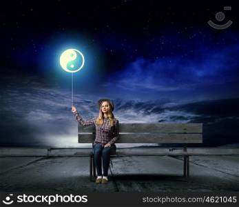 Yin yang concept. Young woman sitting on bench with balloon in hand