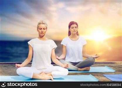 yoga and healthy lifestyle concept - women meditating in lotus pose on wooden pier over sea background. women meditating in yoga lotus pose outdoors
