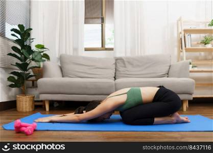 Yoga and wellness concept, Young Asian woman doing yoga to lying in child pose on mat at home.