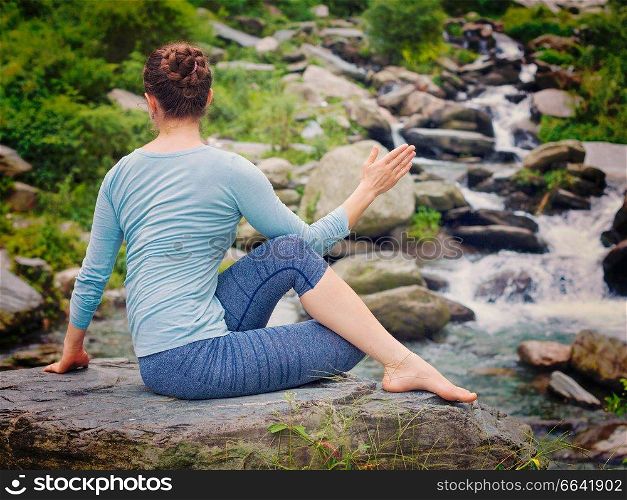 Yoga exercise outdoors -  woman doing Ardha matsyendrasana asana - half spinal twist pose at tropical waterfall in Himalayas in India. Vintage retro effect filtered hipster style image.. Woman doing Ardha matsyendrasana asana outdoors