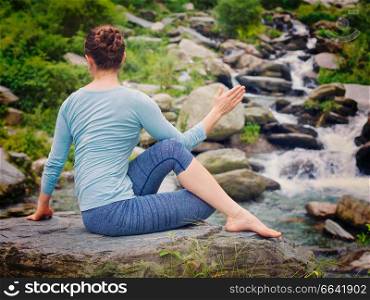 Yoga exercise outdoors -  woman doing Ardha matsyendrasana asana - half spinal twist pose at tropical waterfall in Himalayas in India. Vintage retro effect filtered hipster style image.. Woman doing Ardha matsyendrasana asana outdoors