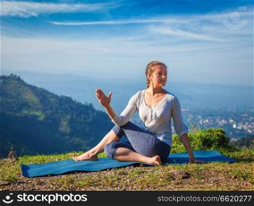 Yoga exercise outdoors -  woman doing Ardha matsyendrasanaasana asana - half spinal twist pose mountains in Himalayas in India in the morning. Woman doing Ardha matsyendrasanaasana asana outdoors