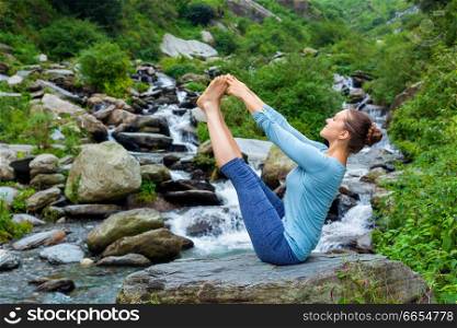 Yoga exercise outdoors -  woman doing Ashtanga Vinyasa Yoga balance asana Ubhaya padangusthasana Big Double Toe Yoga Pose at tropical waterfall in Himalayas in India. Woman doing Ashtanga Vinyasa Yoga asana outdoors