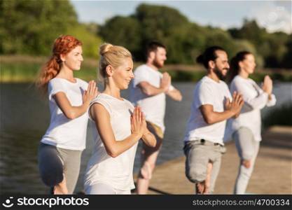 yoga, fitness, sport, and healthy lifestyle concept - group of people in tree pose on mat outdoors on river or lake berth