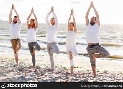 yoga, fitness, sport and healthy lifestyle concept - group of people in tree pose on beach