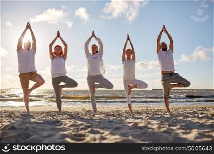 yoga, fitness, sport and healthy lifestyle concept - group of people in tree pose on beach. group of people making yoga in tree pose on beach