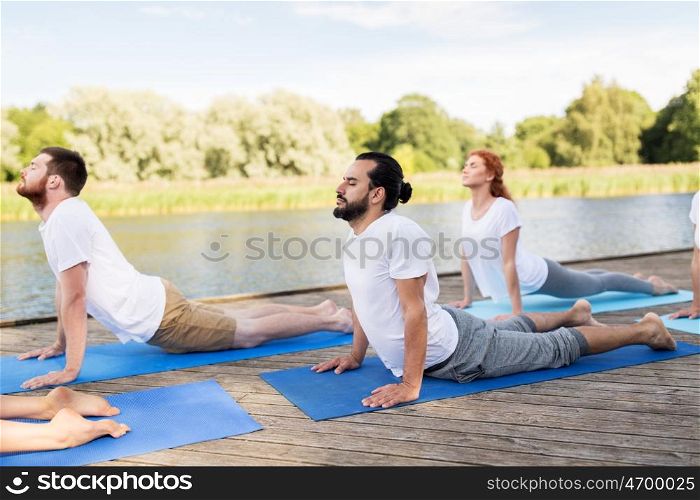 yoga, fitness, sport, and healthy lifestyle concept - group of people making upward facing dog or cobra pose on river or lake berth