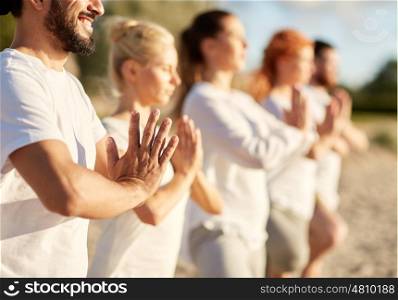 yoga, fitness, sport and healthy lifestyle concept - group of people meditating on beach