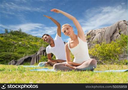 yoga, fitness, sport and people concept - smiling couple making exercises sitting on mats outdoors. smiling couple making yoga exercises outdoors