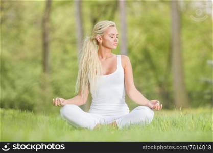 Yoga girl in lotus pose in the park, young woman in white clothes sitting on fresh green grass. Yoga girl in lotus pose in the park