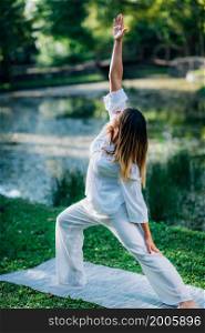 Yoga in nature, young woman in white, peaceful warrior pose, soft green nature background.. Yoga in Nature, Peaceful Warrior Pose.