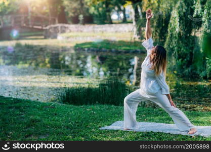 Yoga in nature, young woman in white, peaceful warrior pose, soft green nature background.. Yoga in Nature, Peaceful Warrior Pose.