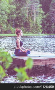 Yoga meditation by Young yogi girl on the pier of a beautiful lake. The concept of appeasement, healthy lifestyle.