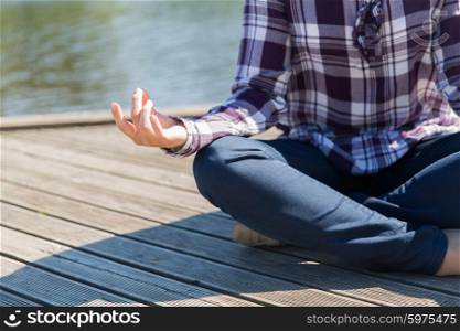 yoga, meditation, people and lifestyle concept - close up of woman meditating in lotus pose outdoors on berth