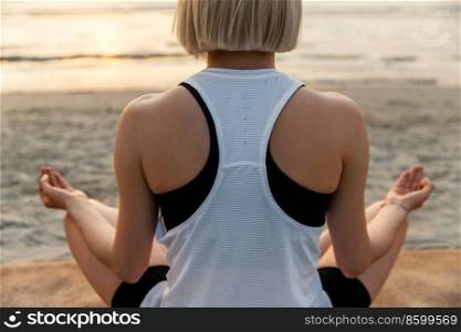 yoga, mindful≠ss and meditation concept - close up of woman meditating in lotus pose on beach over sunset. woman meditating in lotus pose on beach