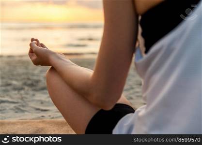 yoga, mindfulness and meditation concept - close up of woman meditating in lotus pose on beach over sunset. woman meditating in lotus pose on beach