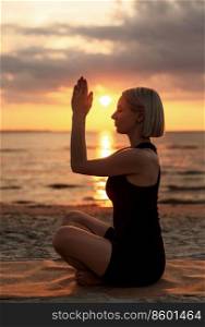 yoga, mindfulness and meditation concept - woman meditating in easy pose on beach over sunset over sunset. woman meditating in easy pose on beach