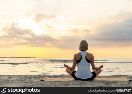 yoga, mindfulness and meditation concept - woman meditating in lotus pose on beach over sunset. woman meditating in lotus pose on beach