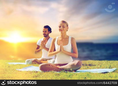 yoga , mindfulness, harmony and people concept - happy couple meditating in lotus pose outdoors over sea background. happy couple making yoga and meditating outdoors