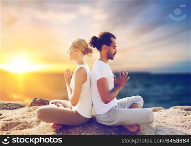 yoga , mindfulness, harmony and people concept - happy couple meditating in lotus pose outdoors over sea background. happy couple making yoga and meditating outdoors