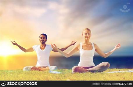 yoga , mindfulness, harmony and people concept - happy couple meditating in lotus pose outdoors over sea background. happy couple making yoga and meditating outdoors. happy couple making yoga and meditating outdoors